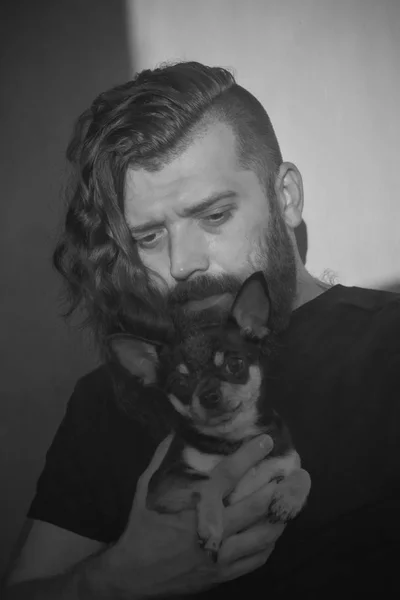 A bearded man hugs a small dog breed Chihuahua.