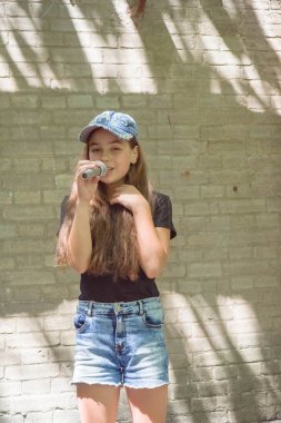 Tuğla duvar arka plan üzerinde mikrofon ile güzel küçük kız