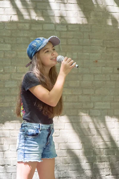 Krásná holčička s mikrofonem na cihlovou zeď pozadí — Stock fotografie