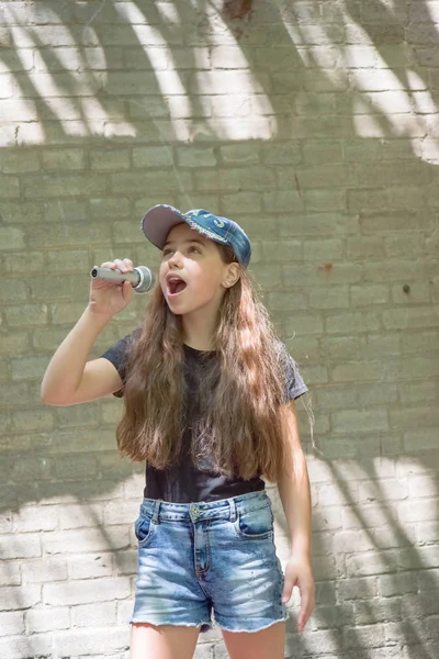 Krásná holčička s mikrofonem na cihlovou zeď pozadí — Stock fotografie