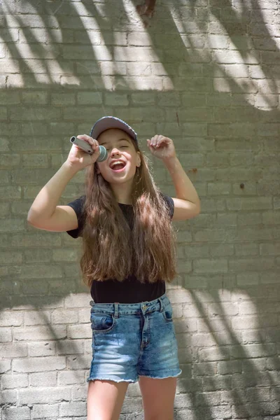 Menina bonita com microfone no fundo da parede de tijolo — Fotografia de Stock