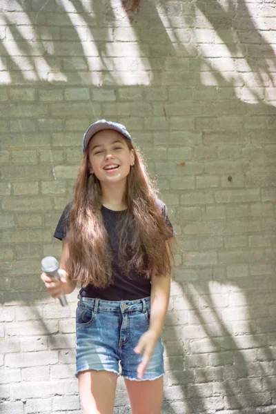 Menina bonita com microfone no fundo da parede de tijolo — Fotografia de Stock