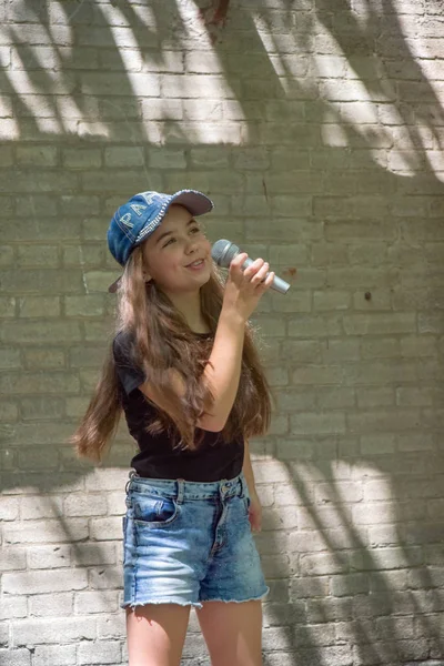 Hermosa niña con micrófono en el fondo de la pared de ladrillo — Foto de Stock