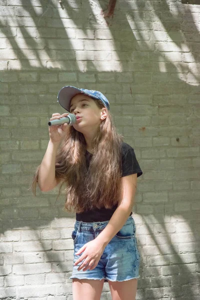 Beautiful little girl with microphone on brick wall background