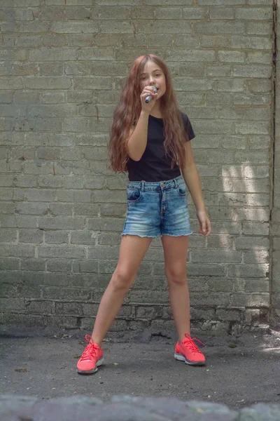 Beautiful little girl with microphone on brick wall background