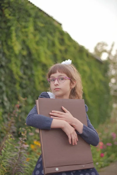 녹지의 배경에 큰 갈색 노트북을 가진 여학생. — 스톡 사진