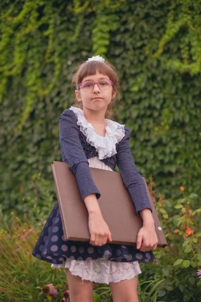 Colegiala con un gran cuaderno marrón sobre un fondo de vegetación . — Foto de Stock