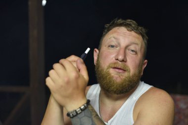 Kırmızı sakallı bir adam elektronik sigara içiyor..