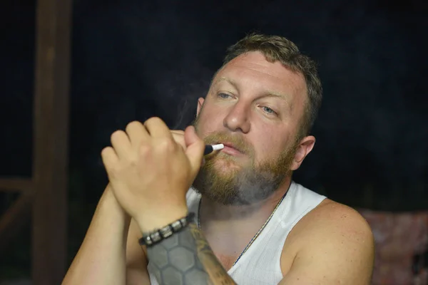 Un bărbat cu barbă roşie fumează o ţigară electronică . — Fotografie, imagine de stoc