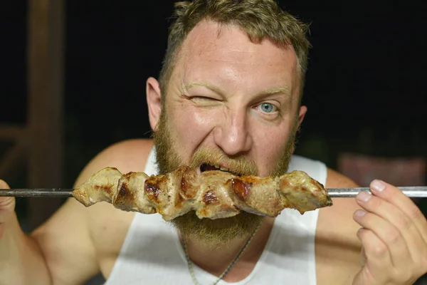 El barbudo come una deliciosa barbacoa. Un hombre con barba roja come brochetas de brochetas —  Fotos de Stock