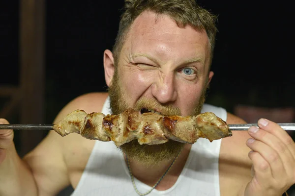 Bearded man eats delicious barbecue. A man with a red beard eats skewers from skewers — Stock Photo, Image