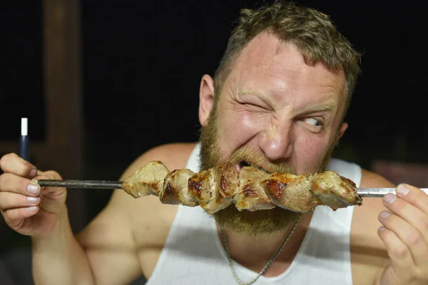 Bearded man eats delicious barbecue. A man with a red beard eats skewers from skewers