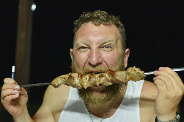 Bearded man eats delicious barbecue. A man with a red beard eats skewers from skewers