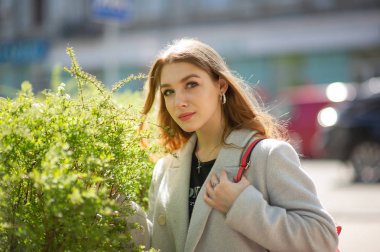 Gri ceketli şık genç güzel kız kameraya bakar ve şehrin arka planına karşı hafifçe gülümser.