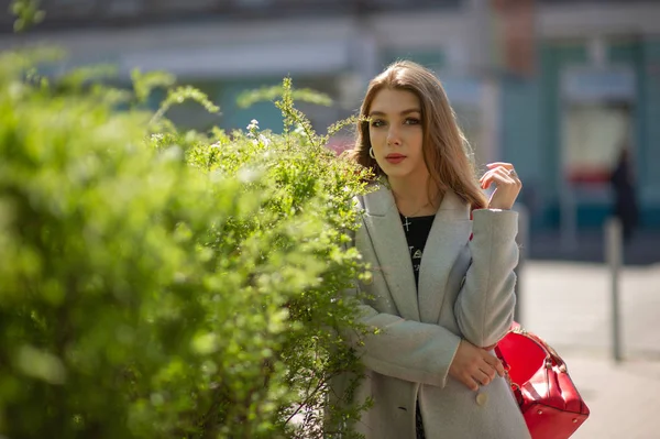 Elegante ragazza carina in un cappotto grigio guarda la fotocamera e sorride leggermente sullo sfondo della città . — Foto Stock