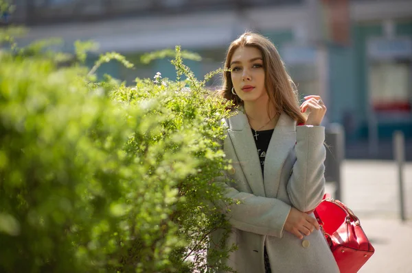 Elegante ragazza carina in un cappotto grigio guarda la fotocamera e sorride leggermente sullo sfondo della città . — Foto Stock