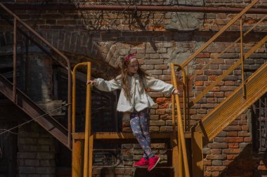 Merdiven korkulukları üzerinde yatan ve aşağı kayan keten elbiseli küçük kız izleme çekim