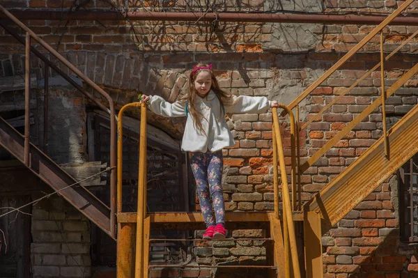 Tracking shot of little girl in linen dress lying on railing of staircase and sliding down
