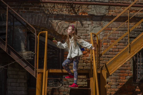 Tracking shot of little girl in linen dress lying on railing of staircase and sliding down