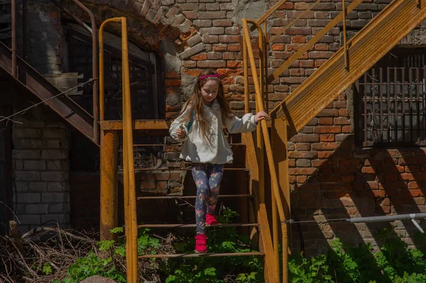 Tracking shot of little girl in linen dress lying on railing of staircase and sliding down