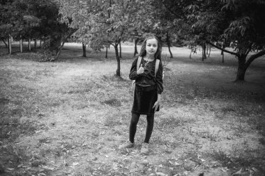 Liseli kız sabah güneşinde okula gider. Okul bahçesinde 9 yaşındaki bir kız öğrenci. Siyah beyaz fotoğraf.