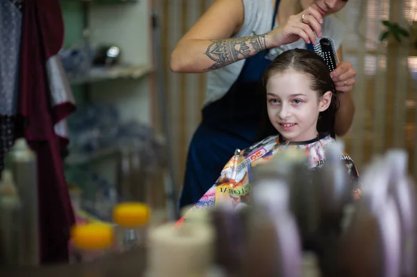 Cabeleireiro estilista faz um penteado para uma menina bonito em um salão de beleza. Cabeleireiro, corte de cabelo . — Fotografia de Stock
