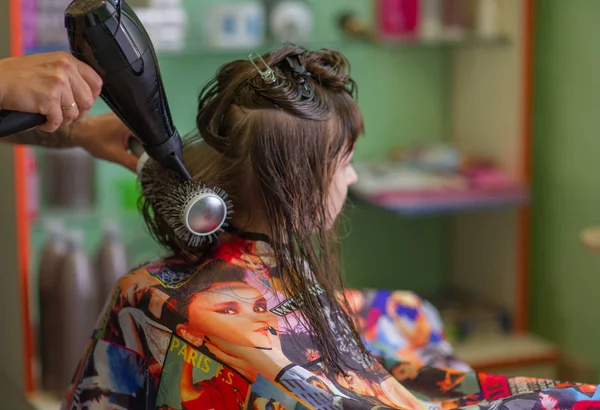 Cabeleireiro estilista faz um penteado para uma menina bonito em um salão de beleza. Cabeleireiro, corte de cabelo . — Fotografia de Stock