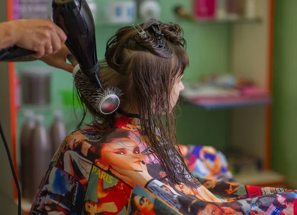 Cabeleireiro estilista faz um penteado para uma menina bonito em um salão de beleza. Cabeleireiro, corte de cabelo . — Fotografia de Stock