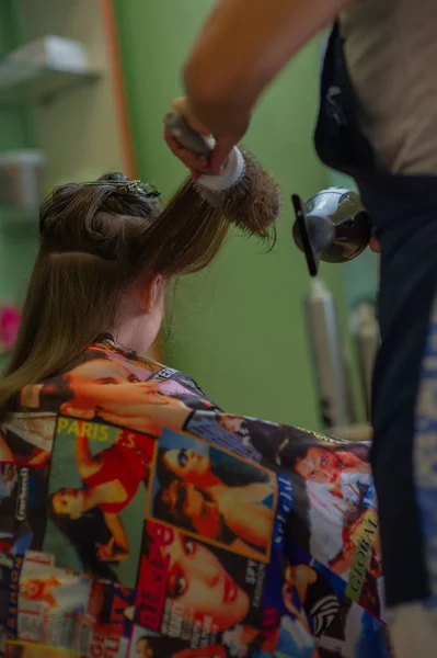 Cabeleireiro estilista faz um penteado para uma menina bonito em um salão de beleza. Cabeleireiro, corte de cabelo . — Fotografia de Stock