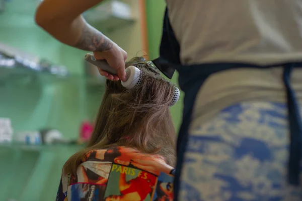 Cabeleireiro estilista faz um penteado para uma menina bonito em um salão de beleza. Cabeleireiro, corte de cabelo . — Fotografia de Stock