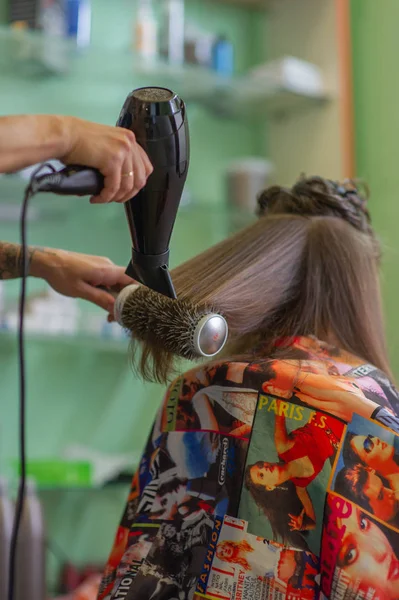 Cabeleireiro estilista faz um penteado para uma menina bonito em um salão de beleza. Cabeleireiro, corte de cabelo . — Fotografia de Stock