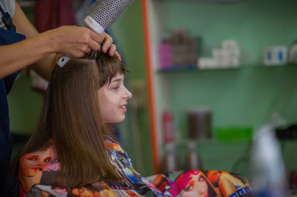 Cabeleireiro estilista faz um penteado para uma menina bonito em um salão de beleza. Cabeleireiro, corte de cabelo . — Fotografia de Stock