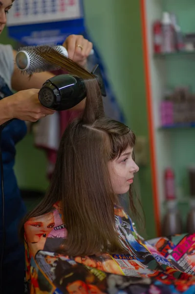 Stylist fodrász teszi a frizurát egy aranyos kislány egy szépségszalonban. Fodrászati, hajvágás. — Stock Fotó