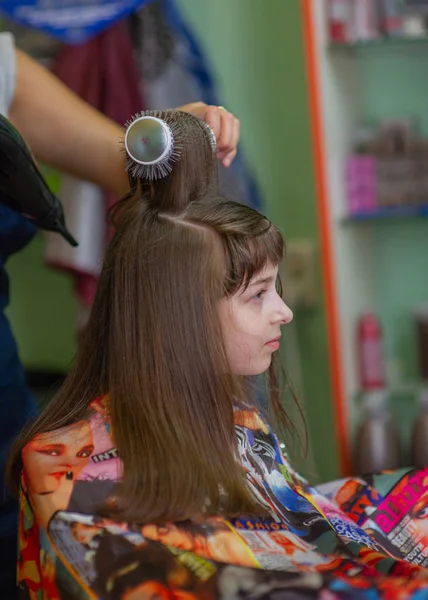 Cabeleireiro estilista faz um penteado para uma menina bonito em um salão de beleza. Cabeleireiro, corte de cabelo . — Fotografia de Stock