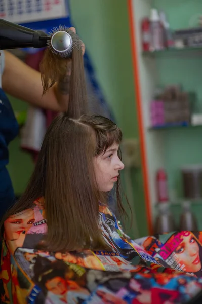 Cabeleireiro estilista faz um penteado para uma menina bonito em um salão de beleza. Cabeleireiro, corte de cabelo . — Fotografia de Stock