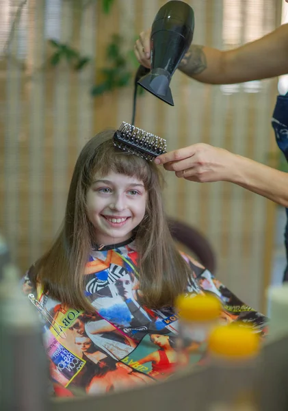 Στυλίστας κομμωτής κάνει ένα χτένισμα για ένα χαριτωμένο κοριτσάκι σε ένα σαλόνι ομορφιάς. Κομμωτήρια, κοπή μαλλιών. — Φωτογραφία Αρχείου