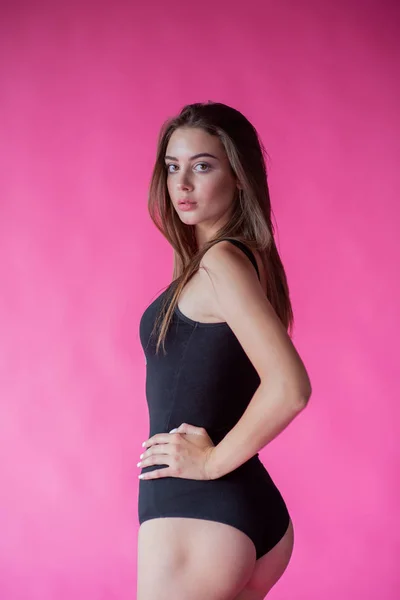 Bella ragazza alla moda con i capelli lunghi in una t-shirt nera. Ragazza in studio su uno sfondo rosa — Foto Stock