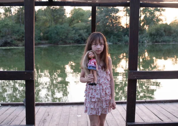 Dívka v šatech, která chodí po promenádě. Malá holčička s panenkou u řeky — Stock fotografie