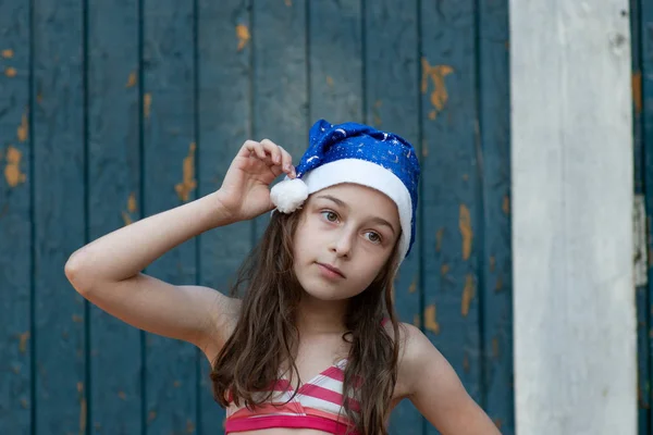Una niña se está divirtiendo y jugando en la víspera de Navidad en el sombrero de Santa Claus, en un traje de baño, un fondo de azul . —  Fotos de Stock