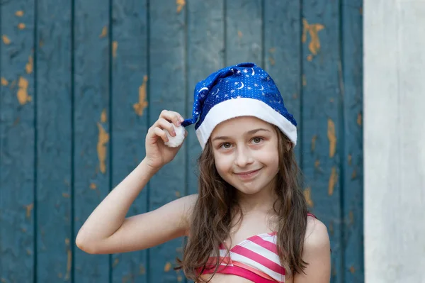 Una niña se está divirtiendo y jugando en la víspera de Navidad en el sombrero de Santa Claus, en un traje de baño, un fondo de azul . —  Fotos de Stock