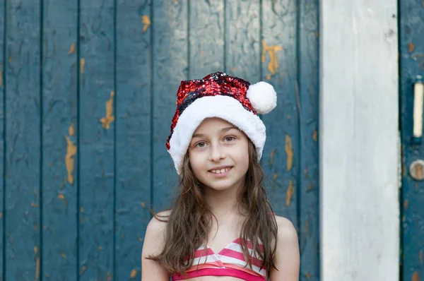 Uma menina está se divertindo e brincando na véspera de Natal no chapéu de Papai Noel, em um maiô, um fundo de azul . — Fotografia de Stock