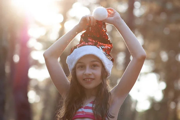 Dítě si zahrává s kloboukem na Santa Clause. Šťastná holčička v Santu v Santa Clause venku v létě . — Stock fotografie