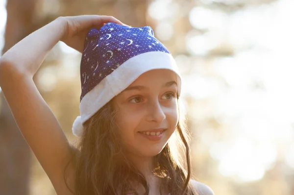 Ein Kind spielt mit einem Weihnachtsmann-Hut. fröhliches kleines Mädchen mit Weihnachtsmann-Hut im Sommer draußen . — Stockfoto