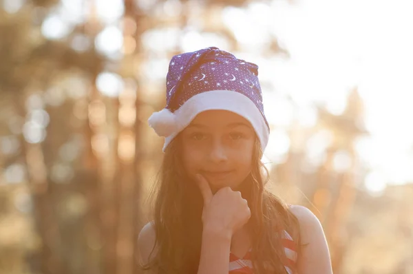 Ein Kind spielt mit einem Weihnachtsmann-Hut. fröhliches kleines Mädchen mit Weihnachtsmann-Hut im Sommer draußen . — Stockfoto