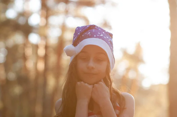 Dítě si zahrává s kloboukem na Santa Clause. Šťastná holčička v Santu v Santa Clause venku v létě . — Stock fotografie