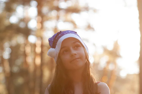 Ein Kind spielt mit einem Weihnachtsmann-Hut. fröhliches kleines Mädchen mit Weihnachtsmann-Hut im Sommer draußen . — Stockfoto