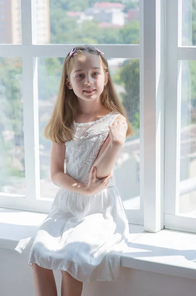 Menina em branco dress.Little menina em um vestido branco pela janela — Fotografia de Stock