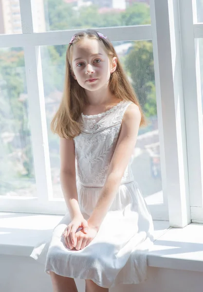 Маленькая девочка в белых платьях. Маленькая девочка в белом платье у окна. — стоковое фото
