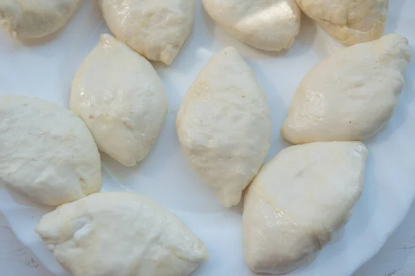 Pasteles de repostería para freír. Pasteles formados con diversos rellenos se encuentran en un plato blanco y están listos para ser fritos en aceite. —  Fotos de Stock