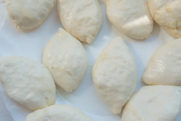 Plăcinte de patiserie pentru prăjit.Plăcinte formate cu diferite umpluturi se află pe o placă albă și sunt gata să fie prăjite în ulei — Fotografie, imagine de stoc